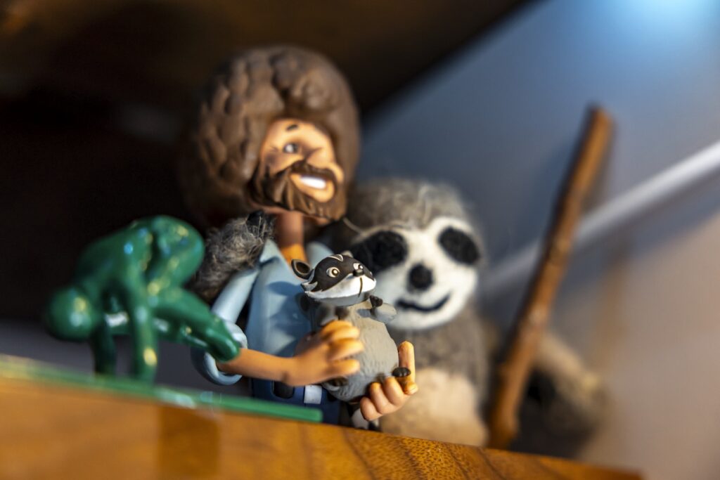 Happy bob ross figurine with a raccoon, frog, and sloth.